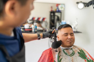 Berber, saçını kestikten sonra bir müşterinin saçını fırçayla temizliyor.