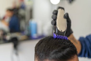 Berber dükkanında saç kesme makinesi kullanan bir erkek berbere yakın plan.