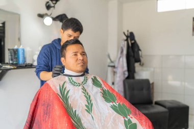 Latin genç berber berber dükkanında bir müşteriye elbise ayarlıyor.