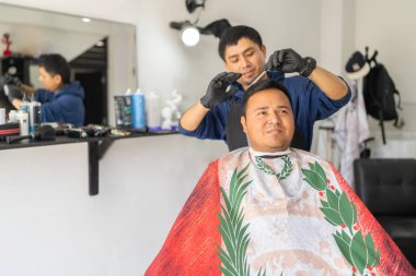 Berber bir müşterinin saçını kesmek için tarak ve makas kullanıyor