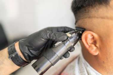 Bir berber dükkanında elle tıraş makinesi kullanan bir müşterinin saçını kesen bir işçinin eline yakın plan.