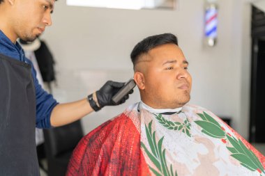 Berber dükkanında rahatça oturan bir müşteriyle ilgilenen Latin berber.