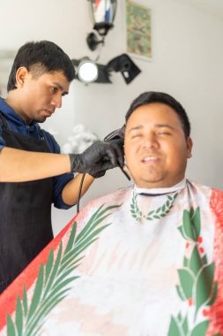 Berberlik yaparken berbere oturmuş gülümseyen bir müşterinin dikey fotoğrafı.