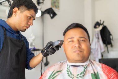 Elektrikli jilet kullanan bir müşterinin saçını kesen konsantre bir kuaför.