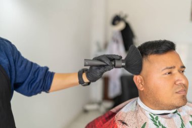 Erkek kuaför saçını kestikten sonra bir müşterinin yüzünü fırçayla temizliyor.