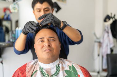 Berber jöle kullanan yeni kesilmiş bir müşterinin saçını düzeltiyor.