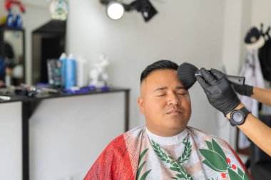 Berber kestikten sonra saçlarını temizlerken gözlerini kapatan bir adam.