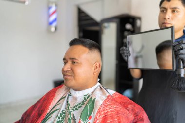 Latin genç berber ayna kullanarak saç kesmesi için sonuçları bir adama gösteriyor.