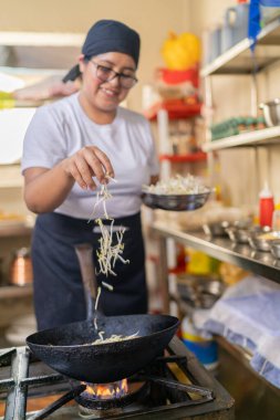 Kızarmış erişteye fasulye filizleri ekleyen bir kadın aşçının dikey fotoğrafı.
