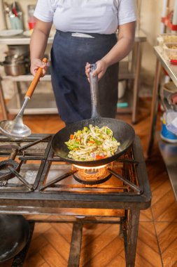 Bir restoranda sebze karıştıran ve pişiren kadın bir şefin dikey fotoğrafı.