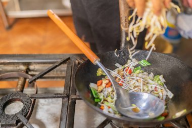 Şef tavaya sebze ve tavukla fasulye filizi ekliyor.