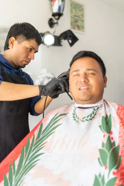 Berberlik yaparken berbere oturmuş gülümseyen bir müşterinin dikey fotoğrafı.