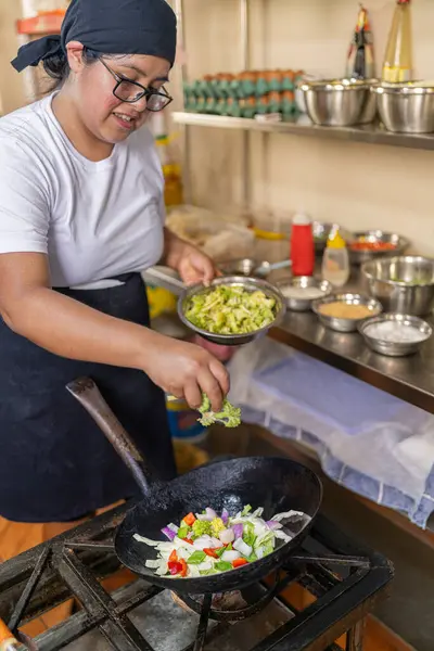 Genç bir aşçının restoranda tavada sebze pişirirken çekilmiş dikey fotoğrafı.