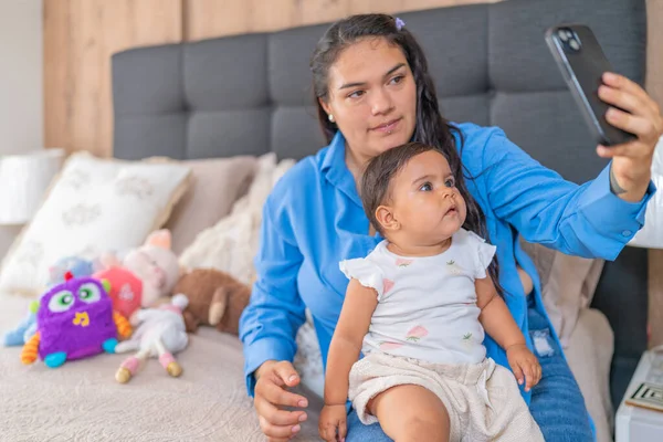 Bir anne bebeğiyle selfie çekmek için bir akıllı telefon tutar; meraklı bir bebek tahtadan bir oyuncakla oynar, duyularını keşfederek.