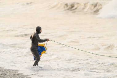 Dalgıç kıyafetli balıkçı deniz suyunun kenarında ağla balık tutuyor.