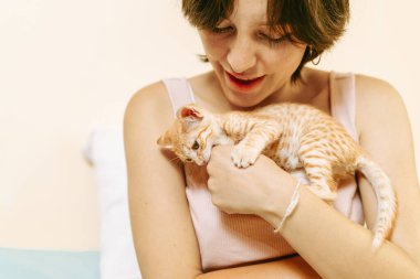 Genç bir bayan kucağında sevimli turuncu çizgili bir kedi yavrusu, sevgi ve özen gösteriyor..