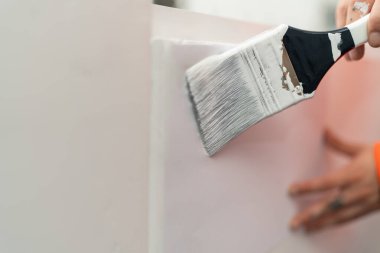 Duvarı beyaza boyamak için boya fırçası kullanan bir elin yakın çekimi.