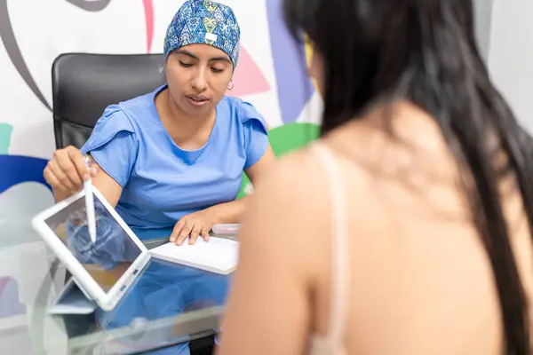 A dentist in scrubs, using a tablet to go over a dental X-ray with her patient in a colorful dental office.