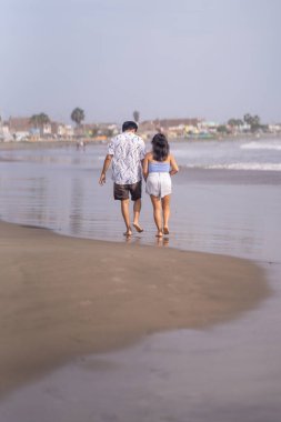 Birbirine aşık çift deniz kıyısında el ele yürüyor, ayaklarını ıslatıyorlar..
