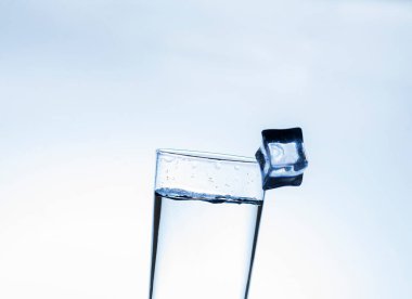 İçme suyunu bardağa doldurmanın görüntüsü, bulanık beyaz arka planda yenilenmiş hissettirir, su sıçratır, köpüklü su