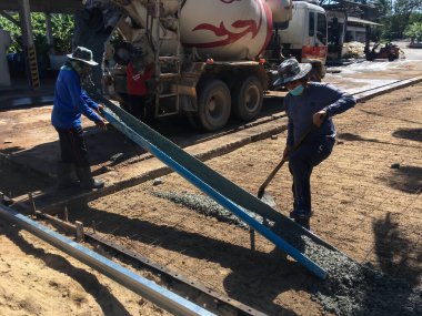 SURATthani, THAILAND - 12 Mayıs 2023: İşçiler kamyonlardan çimento boşaltıyorlar ve onu bölgeye yayıyorlar..