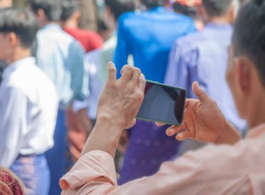 Elinde akıllı telefon taşıyan ve Birmanyalı insanları milli kostüm giydirip, Tayland 'daki Burmalı kardeşlere yönelik Budist Paskalya Perhizi' nin sonunda Kathin festivaline katılmak ve dans etmek için dışarı çıkan bir adam var..