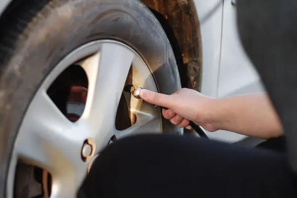 Woman's hand putting air into a car wheel, Car care