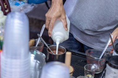Erkek tüccar buzlu sütlü kahve menüsüne karıştırmak için bir şişeye süt döküyor. Soğuk sütlü kahve Tayland 'da popüler bir içkidir.