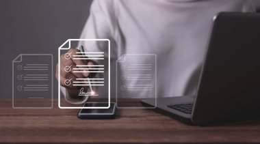 Akıllı cep telefonu ve dizüstü bilgisayarı olan genç bir adam online iş sözleşmesi imzalamak için bir kalem tutuyor, sözleşme imzalıyor, elektronik imza, dijital belgeler, gelecekteki akıllı sözleşmeler.
