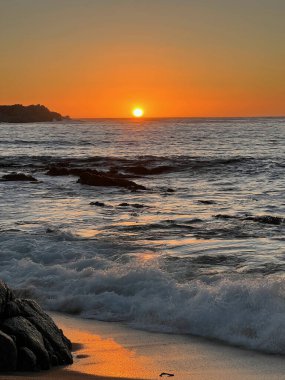 Sıcak tonlarla ve kayalık kıyı manzarasıyla okyanusun üzerinde gün batımı