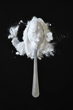 Siyah arka planda bir kaşık kabartma tozu. 