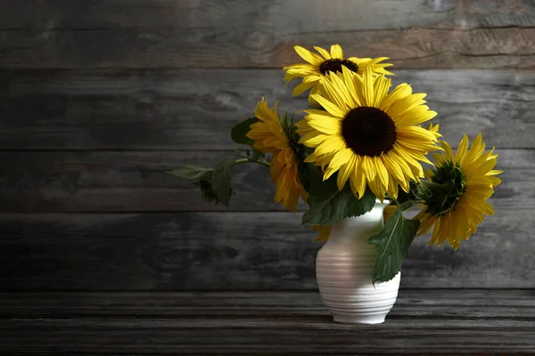 Bouquet of sunflowers in vase. Yellow flower arrangement on wooden background with copy space. Autumn flowers. Fall season.