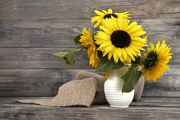 Sunflowers in vase on wooden background with copy space. Autumn festive still life.