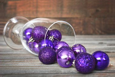 Ahşap arka planda büyük şarap kadehiyle parlayan mor Noel topları. Noel ve Yeni Yıl kavramı.