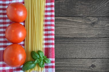 İtalyan yemek geçmişi. Taze domatesler, fesleğen yaprakları, çiğ spagetti ve ahşap masa üzerinde, fotokopi alanı olan damalı kumaş.