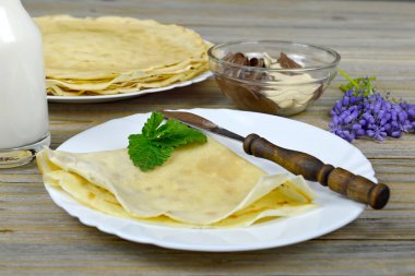 Beyaz tabakta gözleme ve bıçak, tahta masada bir şişe süt ve menekşe çiçeği.