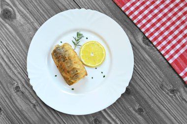 Limon dilimli kızarmış balık filetosu ve beyaz tabakta otlar. 