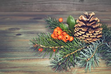 Ahşap arka planda noel süsü, çam kozalağı, yaban mersini ve ladin dalları.