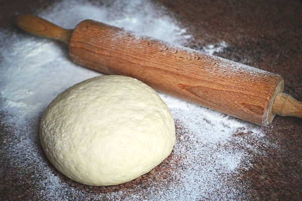 Fresh dough and rolling pin on kitchen board