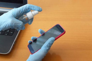 Eldivenli eller telefonu dezenfekte ediyor. Virüs salgını önleme. Virüs koruması