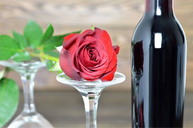 Kırmızı gül, iki şarap kadehi ve ahşap arka planda bir şişe kırmızı şarap.