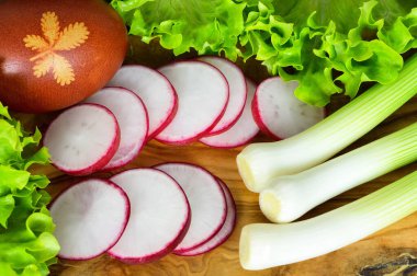 Yeşil soğan, kırmızı turp, marul ve ahşap arka planda renkli Paskalya yumurtası.