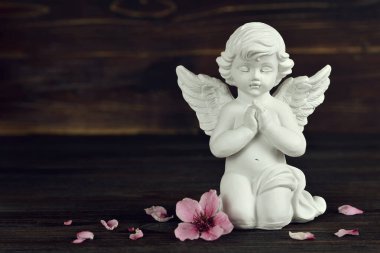 Koruyucu melek diz çöküp dua ediyor ve çiçek yaprakları ahşap arka planda 