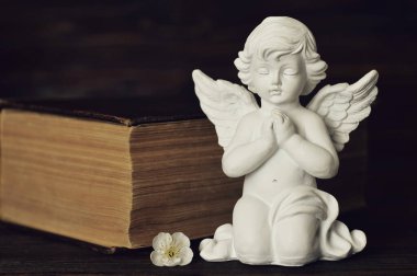 Koruyucu melek diz çöküp eski kitabın arka planında dua ediyor 