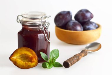 Kavanozda erik reçeli, kaşık, nane yaprakları ve beyaz arka planda taze erikler.