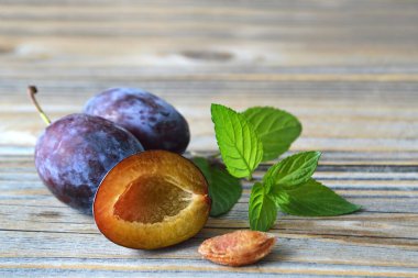 Tahta zemin üzerinde nane yaprakları olan taze erik meyveleri.