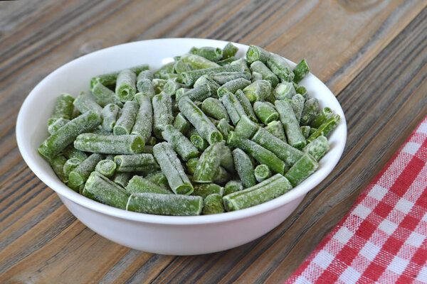 Замороженные зеленые бобы в миске, деревянный фон