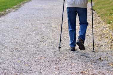 Adam parkta bastonla yürüyor.