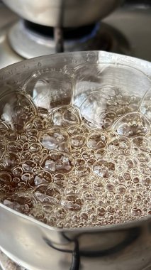 Küçük bir tencerede kaynayan karamelli yakın çekim. Karışım ısındıkça kabarcıklar oluşuyor. Karamel 'in zengin, altın rengi tencerenin yüzeyine zıt, bu klasik ikramı yapmanın tatlı ve hoşgörülü sürecini yakalıyor..