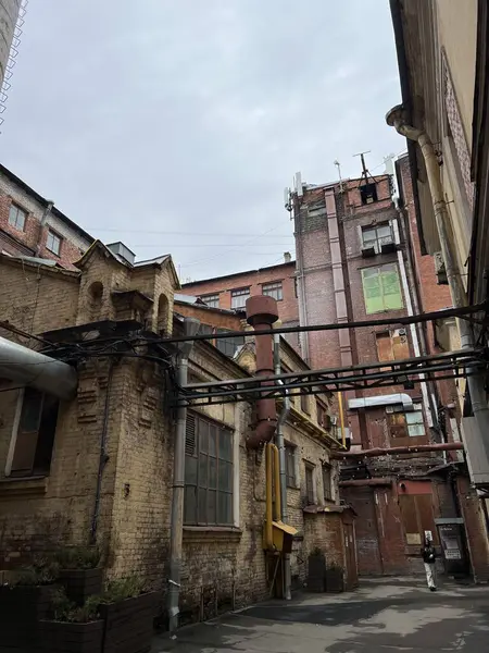 Tuğla binaları, metal boruları ve yıpranmış pencereleri olan eski bir sanayi avlusu. Tarih ve kentsel bozulmanın bir karışımı, unutulmuş bir endüstriyel çağın atmosferini yakalıyor. Arka planda yalnız bir kişi bir ölçek ve gizem duygusu ekler..